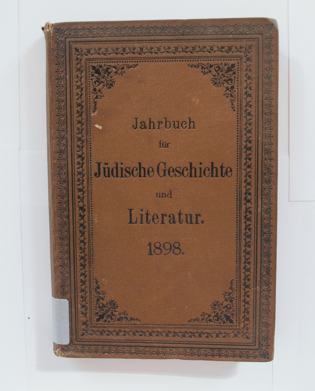 [Translate to English:] Cover des Buches zeigt maronenbraunen Umschlag und Titel des Buches, kunstvoll gerahmt in eine schwarze Bordüre, welche sich über den gesamten Rand erstreckt.