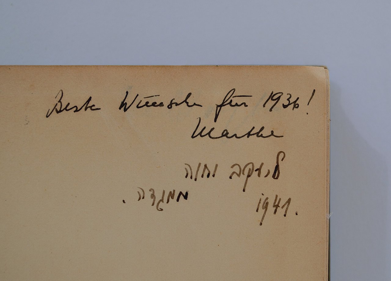 [Translate to English:] Vorsatz mit zwei Widmungen, eine in lateinischer, die andere in hebräischer Schrift. Die erste widmung besagt: "Beste Wünsche für 1936! Marthe". Die zweite Widmung auf hebräisch besagt: "Für Jacob und Eva 1941 von Magda" Die erste Widmung ist vermutlich für einen Vorbesitzer oder Vorbesitzerin bestimmt, die zweite richtet sich direkt an das Ehepaar Toury.